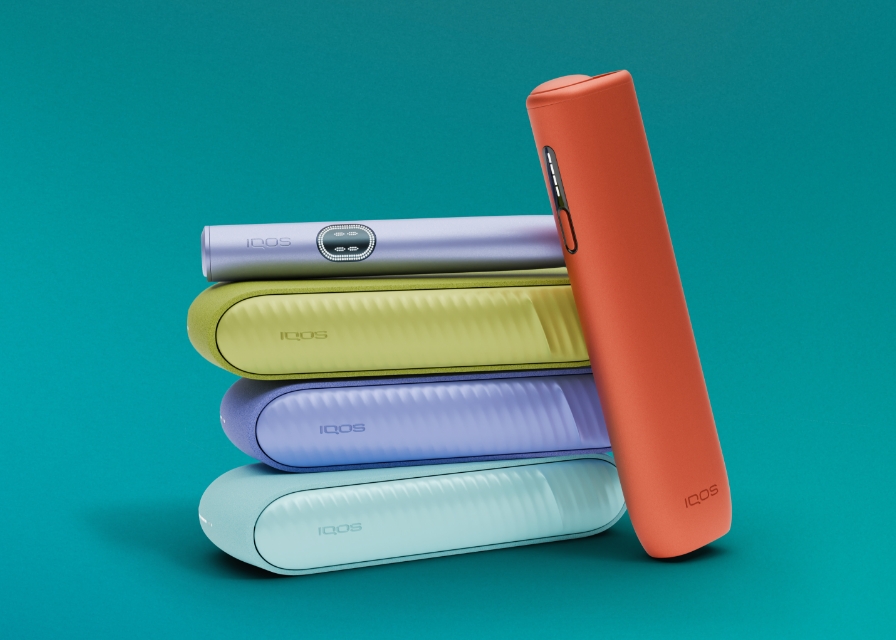 Três equipamentos IQOS ILUMA i na cor azul claro, violeta e verde sobrepostos, com dispositivo IQOS ILUMA i violeta no topo e equipamento IQOS ILUMA i ONE terracota encostado e orientado para a esquerda, em fundo azul