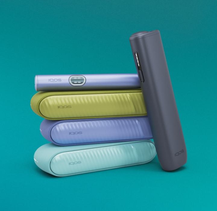Três equipamentos IQOS ILUMA i na cor azul claro, violeta e verde sobrepostos, com dispositivo IQOS ILUMA i violeta no topo e equipamento IQOS ILUMA i ONE terracota encostado e orientado para a esquerda, sobre fundo azul