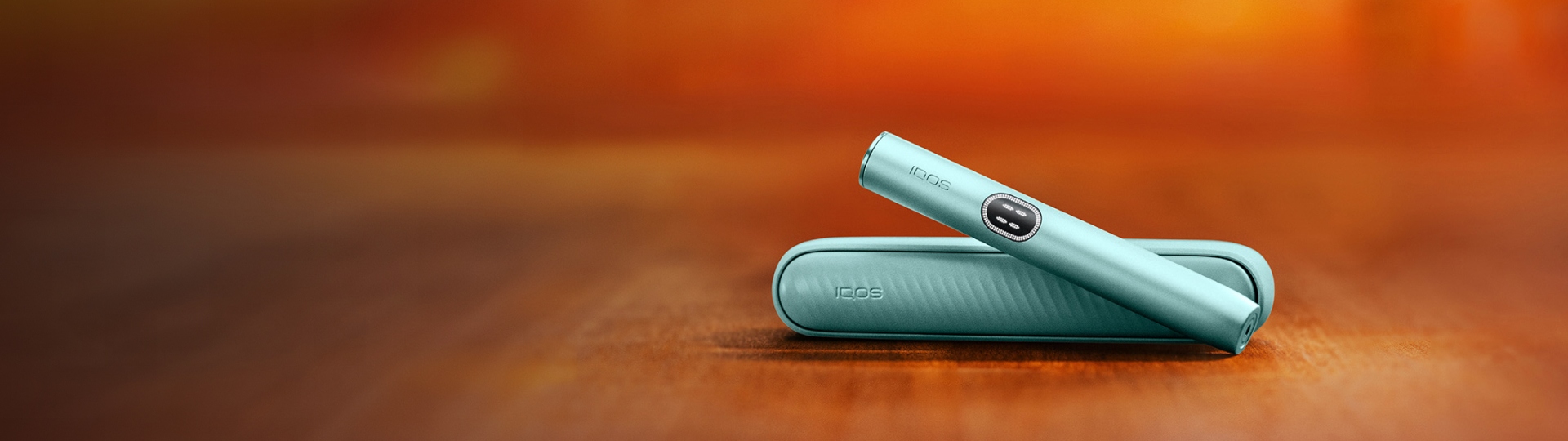 Dispositivo IQOS ILUMA i Azul Claro sobre carregador de bolso, em fundo desfocado

