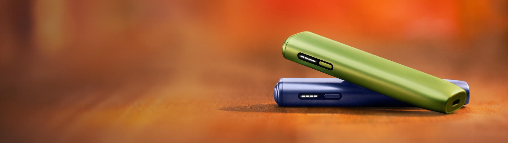 Dispositivo IQOS ILUMA i ONE Verde sobre dispositivo IQOS ILUMA i ONE Violeta, em fundo vermelho 
