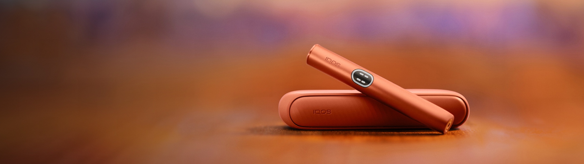Dispositivo IQOS ILUMA i Terracota sobre carregador de bolso, em x, em fundo vermelho