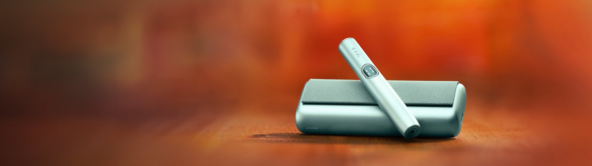 Dispositivo IQOS ILUMA i PRIME Azul Claro com Stick sobre carregador de bolso, em fundo exterior desfocado