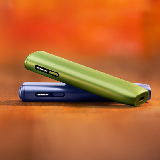 Dispositivo IQOS ILUMA i ONE Verde  sobre dispositivo ILUMA i ONE violeta, em fundo vermelho