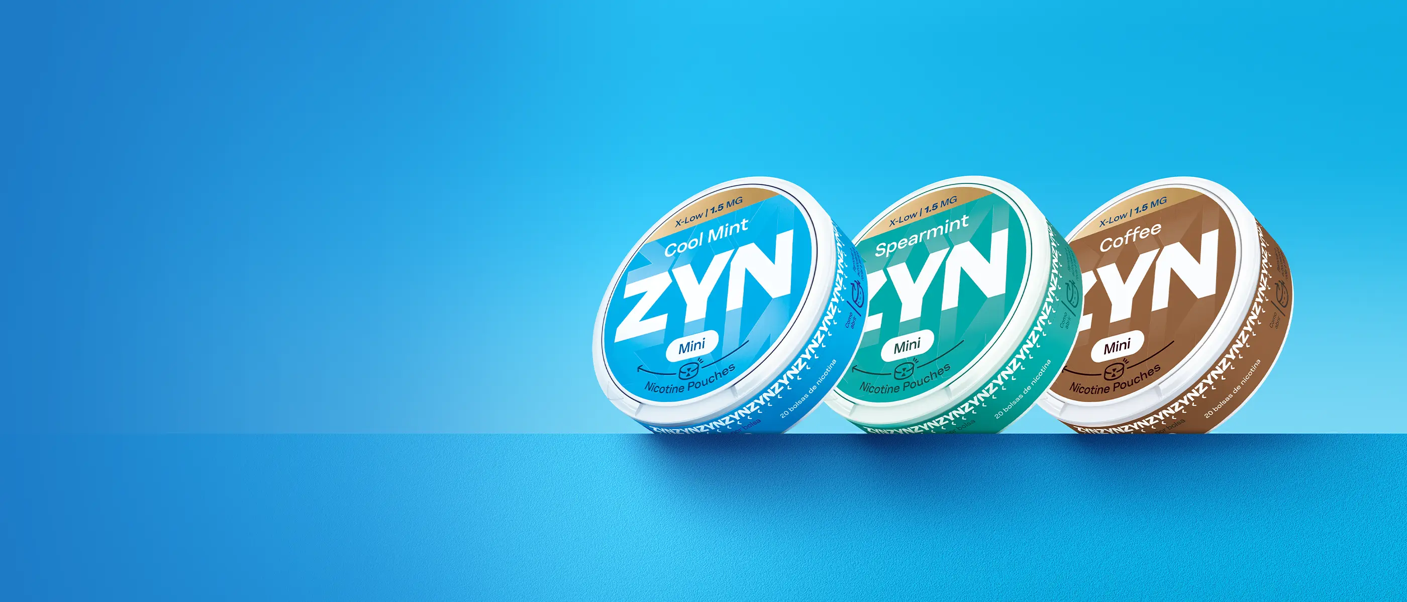 Grande plano de três embalagens de ZYN, ZYN Cool Mint X-Low 1,5 MG Mini, ZYN Spearmint X-Low 1,5 MG Mini e ZYN Coffee X-Low 1,5 MG Mini, sobre fundo azul.