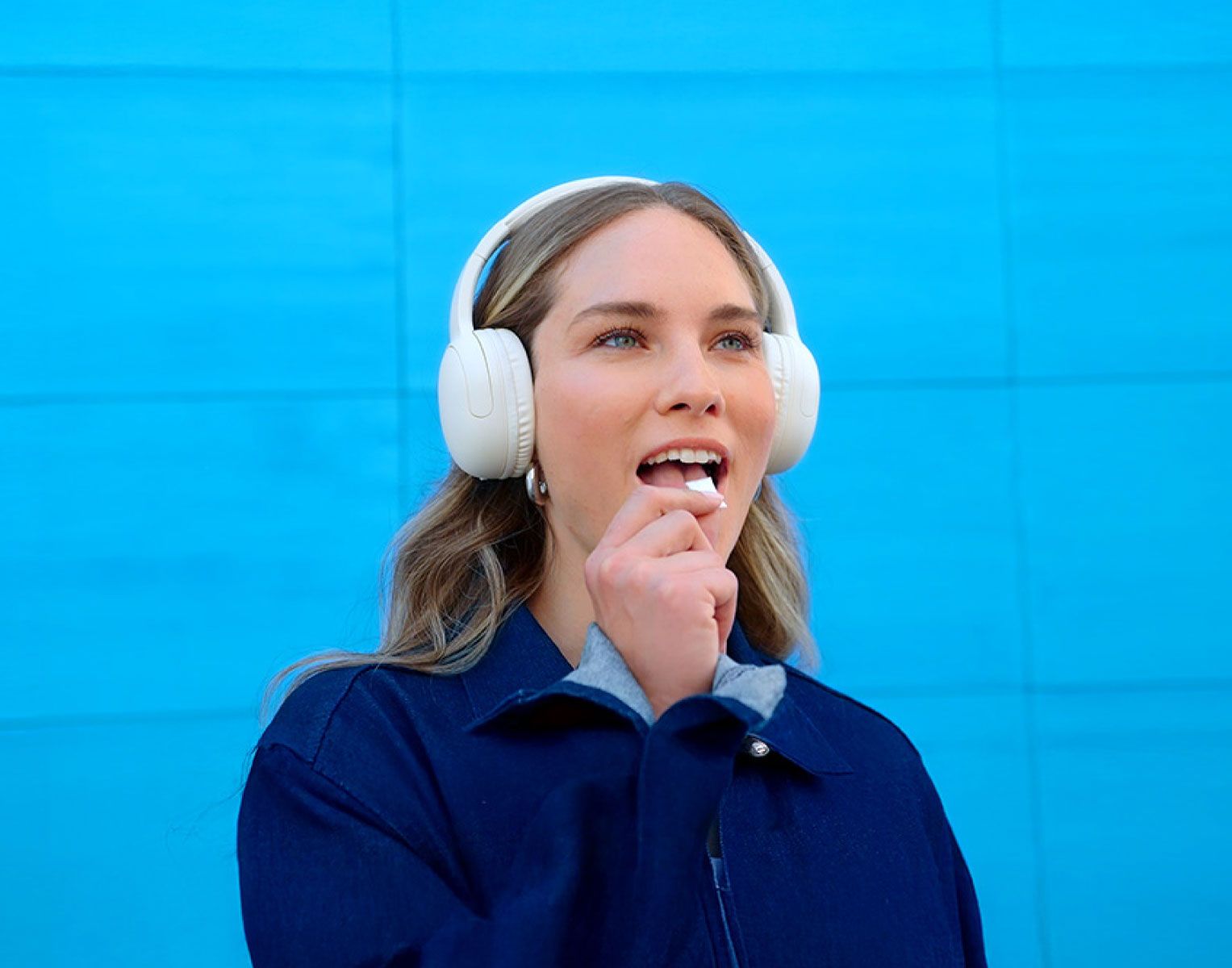 Mulher com auscultadores brancos com fundo azul a colocar uma bolsa de ZYN na boca