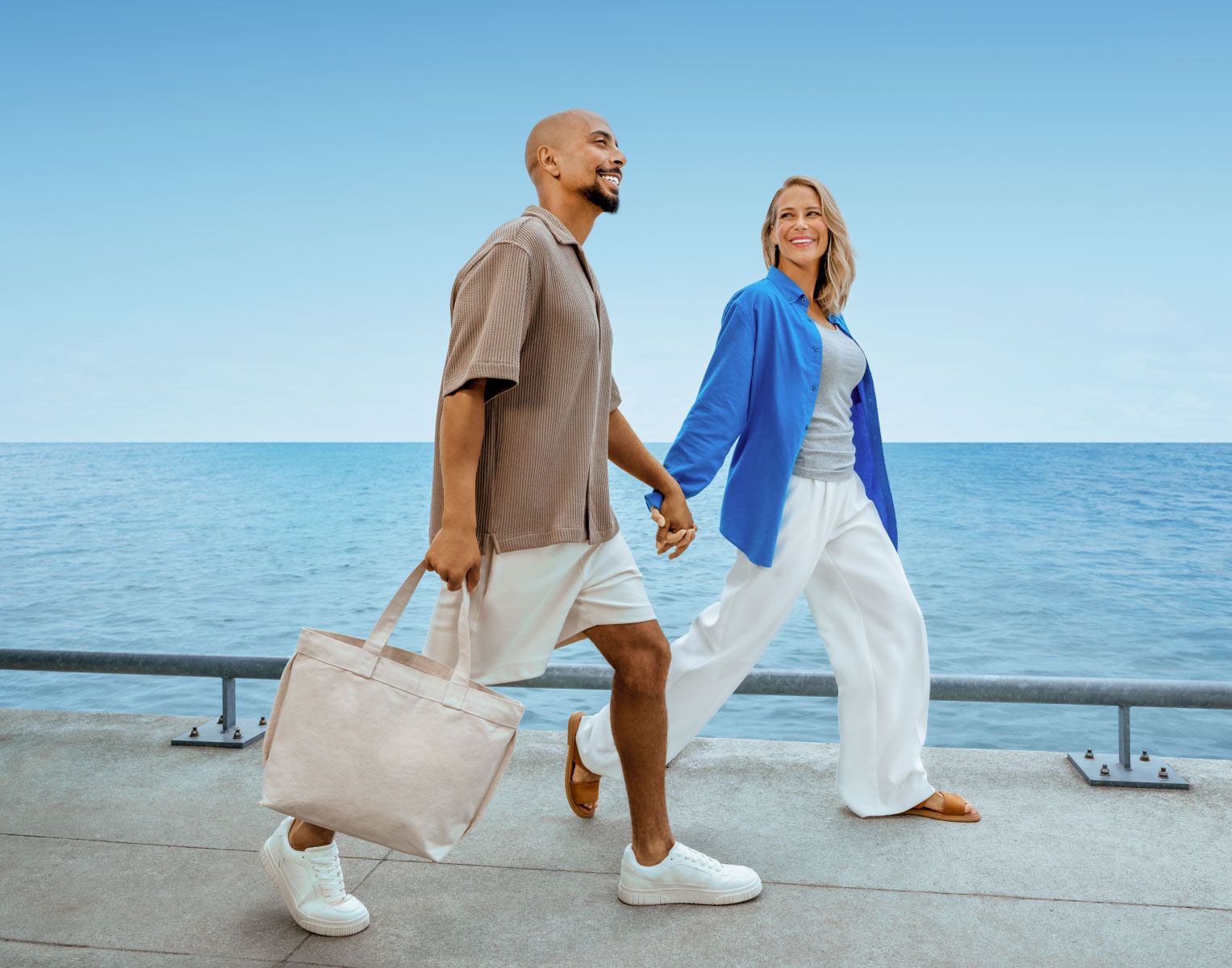 homem e mulher a passear de mão dada num pontão perto do mar