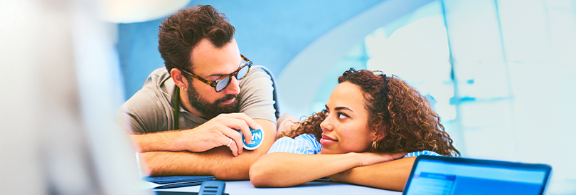 Homem e mulher apoiados num balcão de loja, estão a olhar um para o outro e o homem tem uma lata de ZYN azul na mão. O homem usa óculos e a mulher uma bandelete para o cabelo