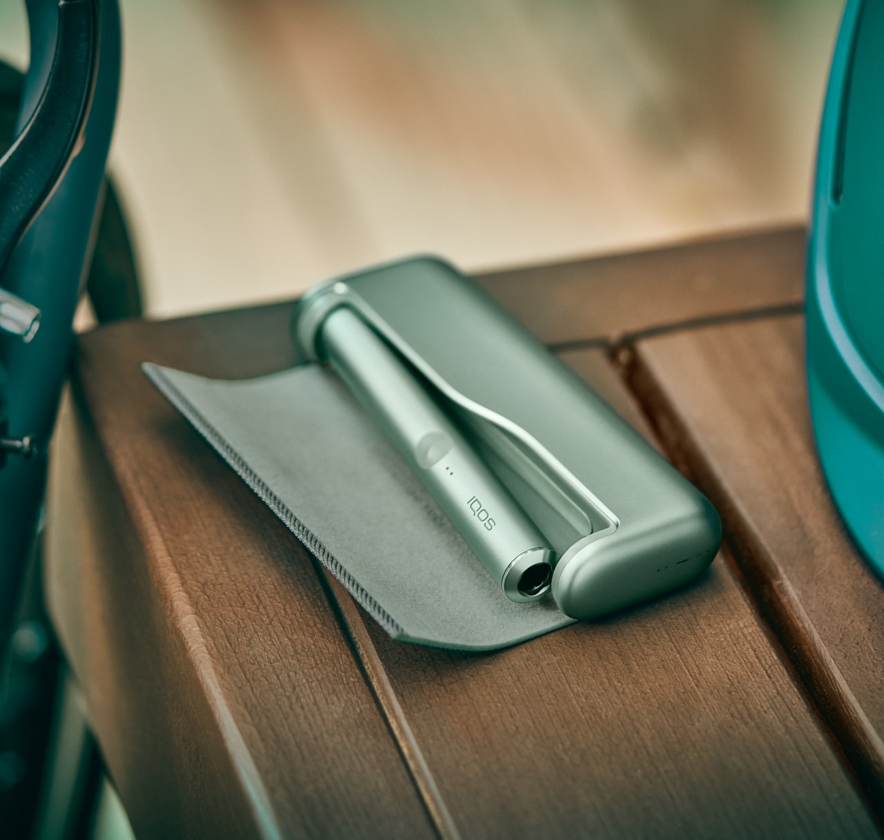 A moss green IQOS ILUMA device and charger resting on a table.