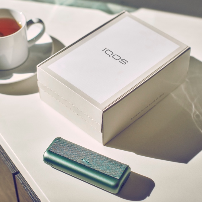 IQOS 3 DUO dourado fora da sua embalagem sobre uma mesa de madeira.