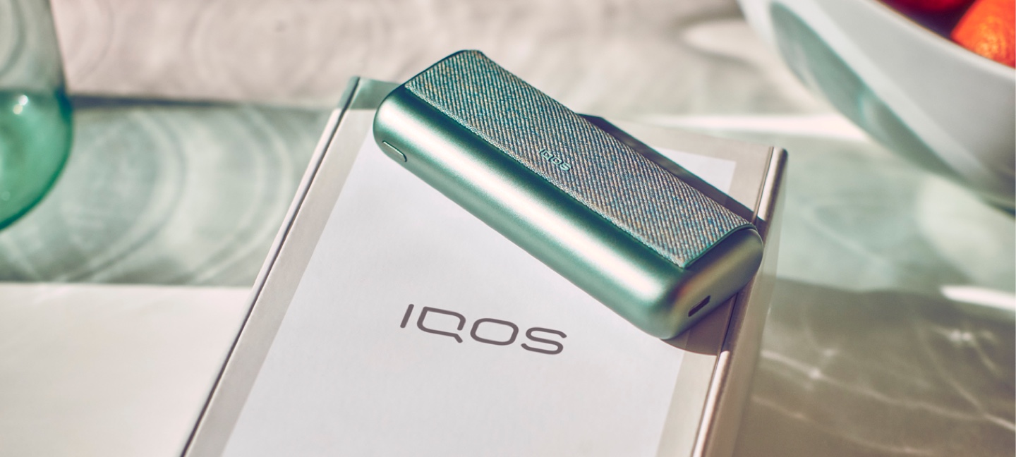 Um dispositivo IQOS 3 DUO dourado num livro de cópias cor-de-laranja.