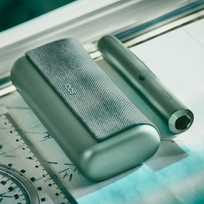 Jade green IQOS ILUMA device and charger on a desk.