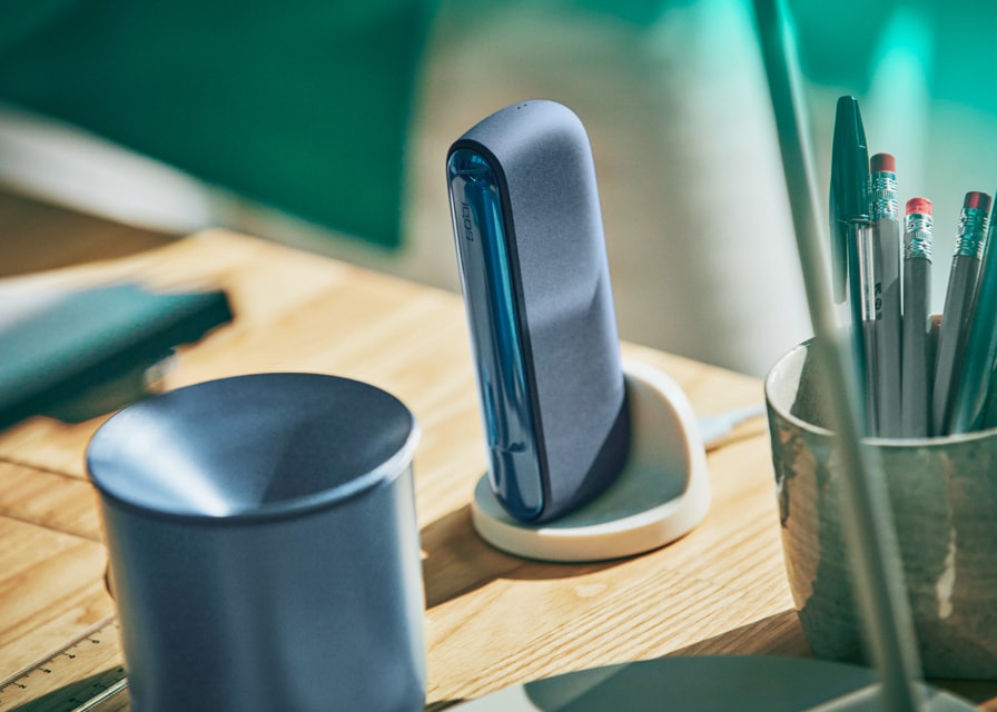 Um Recipiente IQOS e um IQOS ILUMA a carregar numa Base de Carregamento IQOS