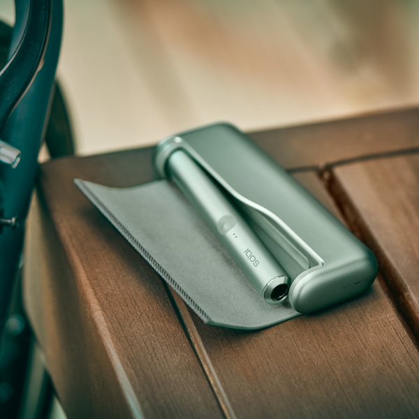 A Jade Green IQOS ILUMA PRIME Holder and Pocket Charger in a person's hands.