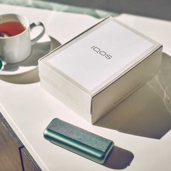 Um equipamento IQOS junto a uma caixa IQOS fechada.