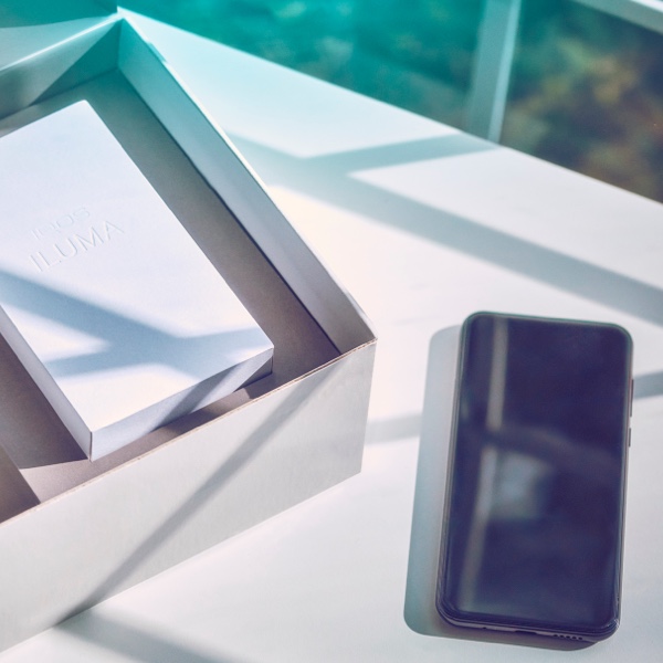 A smart phone next to an open IQOS box on a table.