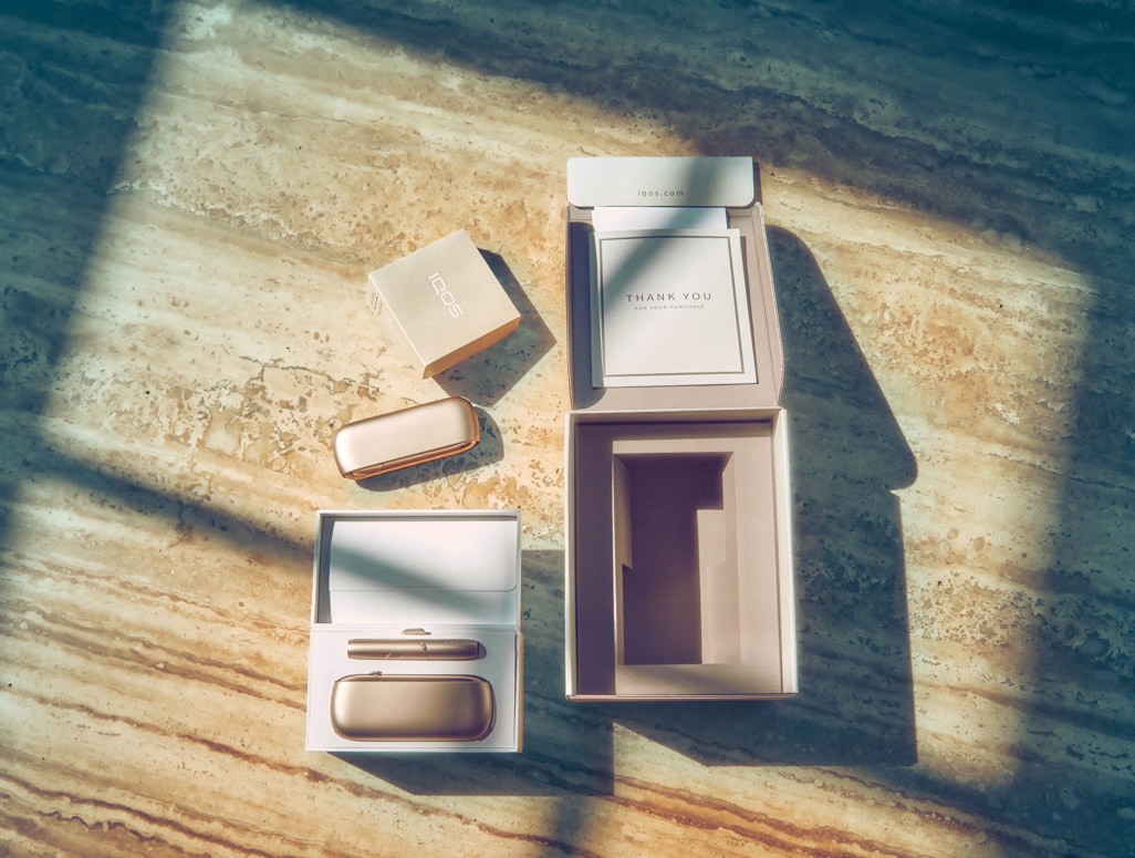 IQOS 3 DUO dourado fora da sua embalagem sobre uma mesa de madeira.
