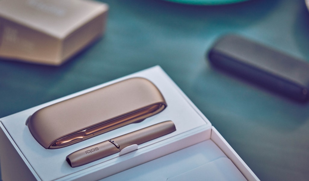 IQOS 3 DUO dourado na sua embalagem sobre uma mesa azul