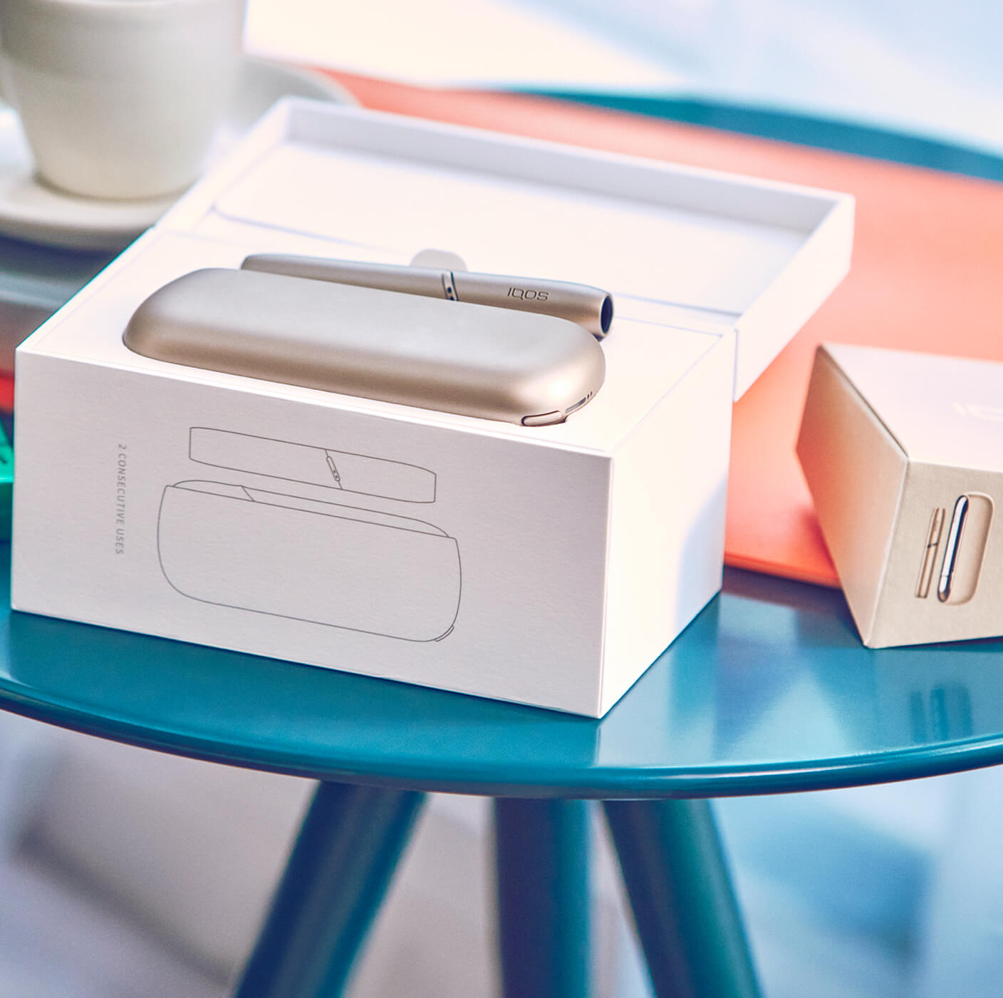 A new gold IQOS device displayed in its packaging on a blue stool