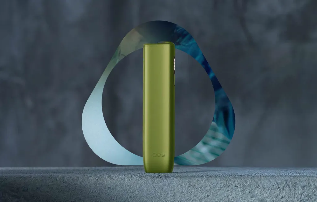 Dispositivo IQOS ILUMA i ONE verde centrado num fundo cinzento escuro. Logótipo IQOS na imagem.