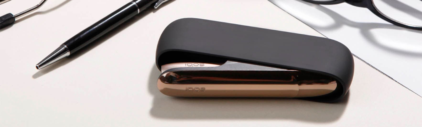 Open IQOS 3 black charger with golden door and golden device on a desk